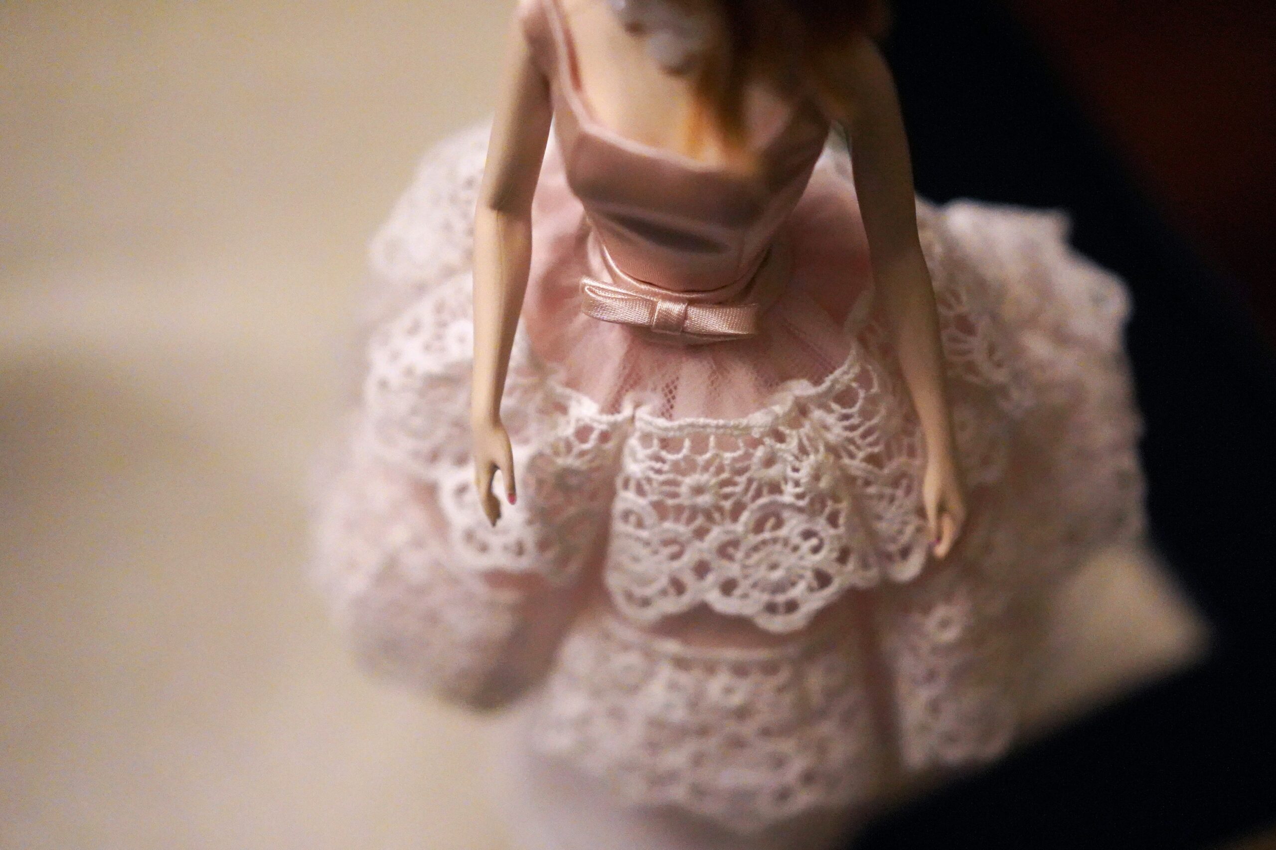 The body of a modern toy doll wearing a light pink dress with white lace.